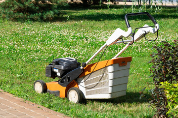 Fototapeta premium A lawn mower on a lush green lawn surrounded by flowers. The back yard of the house