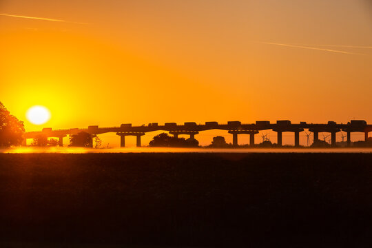 Sunrise over Ouse Bridge, M62, Goole, East Yorkshire during the heat wave in August 2022, with mist rising and wind turbines in the background.  Horizontal.  Copy space