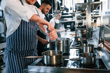 Boiling and adding ingredients. Kitchen workers is together preparing the food