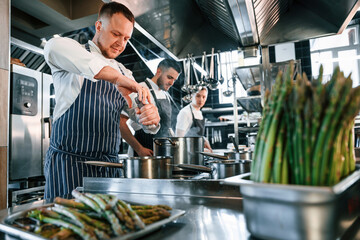 Boiling and adding ingredients. Kitchen workers is together preparing the food