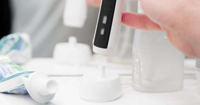 Electric toothbrush charging in bathroom. Ultrasonic toothbrush on wireless charger in bathroom. Smart black and white electric brush with colorful bristle for oral hygiene and cavity prevention.