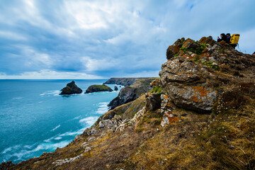 Hikers look out over a rocky coastline on a cloudy day, Cornwall UK