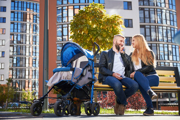 Happy family sitting together with unrecognizable baby in blue pram at modern courtyard of city...