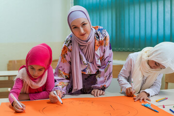 Group of happy Muslim school kids with their teacher working on project together at classroom.