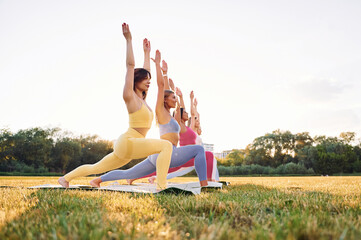 Doing warrior pose. Group of women have fitness outdoors on the field together