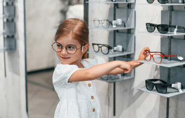 Fototapeta na wymiar Many of the products. Little girl in the glasses store choosing eyewear