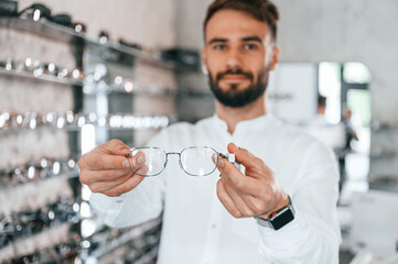 Big choice. Stylish man with beard choosing glasses in the optics store