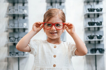 Portrait of little girl that is in the glasses store choosing eyewear