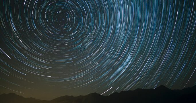 Timelapse of silhouetted mountains with circumpolar star trails in northern sky