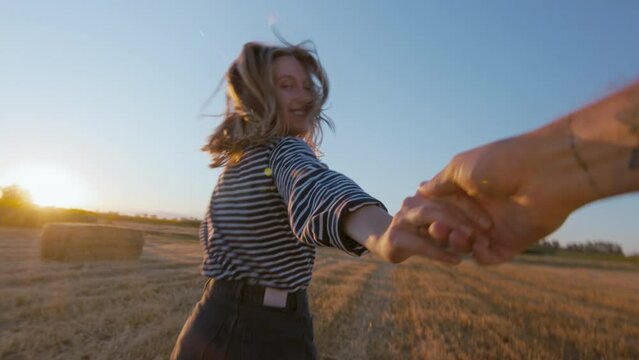 Handheld authentic shot of young woman run away from camera and look back. POV couple in love in summertime outdoor freedom in field. Commercial happiness concept. Millennial relationship lifestyle