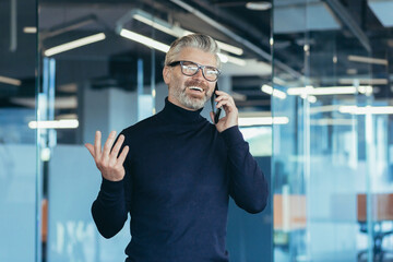Senior gray haired businessman owner talking on phone in modern office, successful investor smiling in glasses