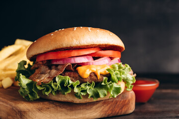 Delicious burger with beef and crispy bacon and potatoes fries on a dark background