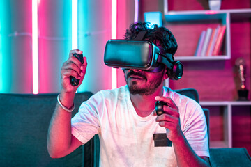 Naklejka premium Focus on VR, Young gamer playing video game on virtual reality or VR headset using joystick at home - concept of metaverse, cyberspace and futuristic.