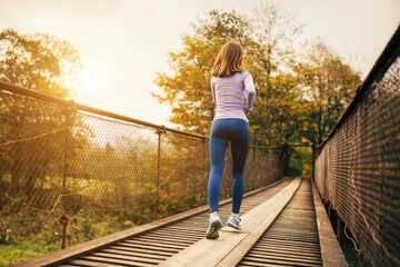 Rear view of a young female athlete jogging in the morning on the bridge.