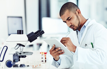 Serious male scientist working on a tablet reviewing an online phd publication in a lab. Laboratory...