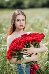 A beautiful girl poses in a field of flowers with a bouquet of red roses