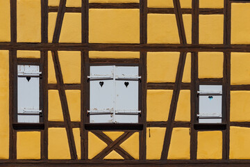 A fragment of a bright yellow wall with brown wooden partitions and windows with closed white shutters of traditional fairy houses in the village of Alsace, Colmar, France