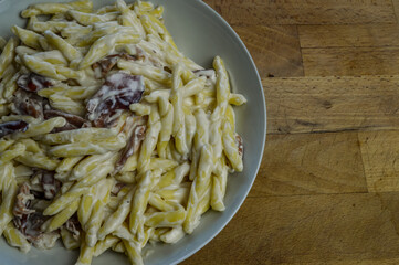 strozzapreti cream and speck, specialty from northern Italy, fresh twisted pasta with sauce made of fresh cream and speck, a smoked ham, and parmesan - in a white plate on a wooden cutting board