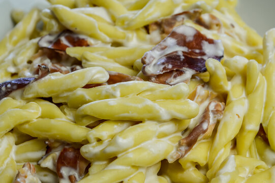 strozzapreti cream and speck, specialty from northern Italy, fresh twisted pasta with sauce made of fresh cream and speck, a smoked ham, and parmesan - close up