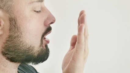 Bad breath. The concept of halitosis. A young man checks his breath with his hand