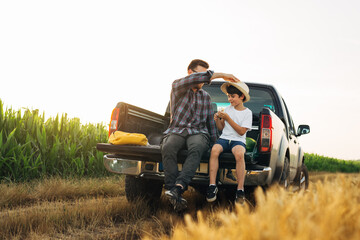 father and son sits on trunk of car in wheat and corn field