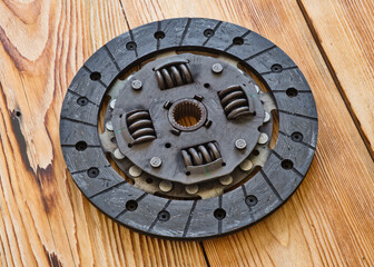 Old and worn out car clutch disk on wooden background close-up. Old automobile spare part.