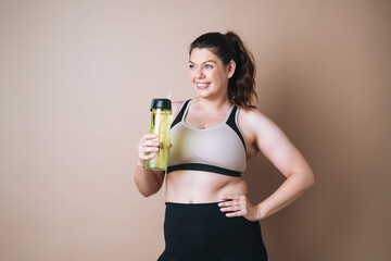 Self loving young woman plus size in sport with bottle of water on beige background, body love