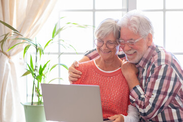 Beautiful caucasian senior couple with eyeglasses browsing together on laptop sitting at home, old...