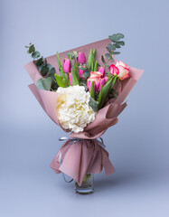 Handmade bouquet for Mother's Day in a festive paper package stands in a vase on a blue background.