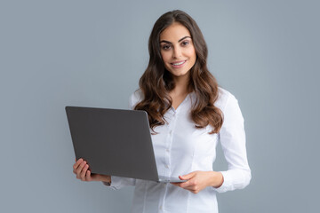 Portrait of a cheerful young casual girl standing isolated over gray background, using laptop computer. Business woman at work.