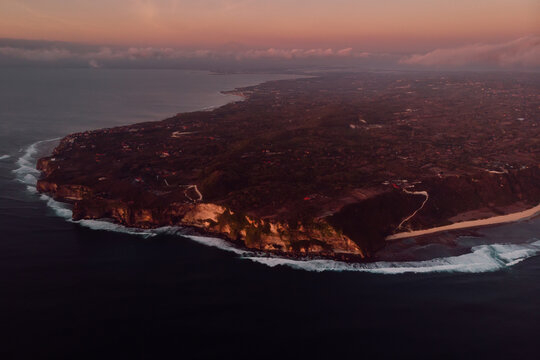 Aerial view of peninsula with cliff and ocean with warm sunset in Bali