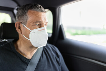 Senior in his 70s sitting at the back of car wearing a face mask