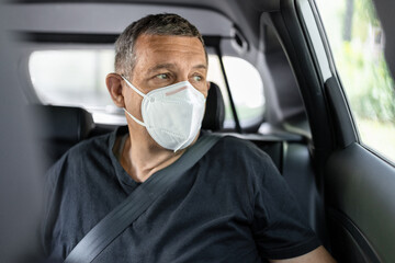 Fototapeta na wymiar Senior in his 70s sitting at the back of car wearing a face mask