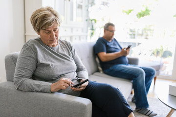 Senior couple using their mobile phones at home