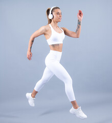 Fototapeta na wymiar Sporty fitness woman with headphones runner stretching legs before run. Sporty woman runner on gray background. Dynamic movement. Sport music.