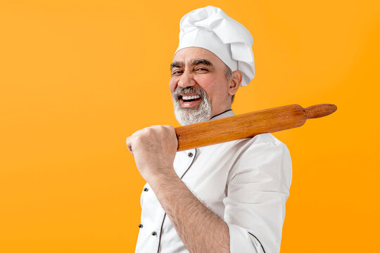 Chef-cooker in a chef's hat and jacket with wood rolling pin. Senior professional baker man wearing a chef's outfit. Character kitchener, pastry chef for advertising