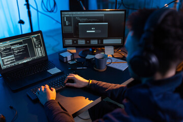 cybercrime, hacking and technology concept - close up of male hacker in dark room writing code or using computer virus program for cyber attack