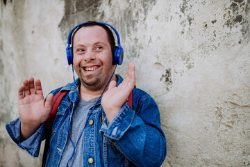 Close-up portrait of happy young man with Down sydrome listening to music when walking in street.