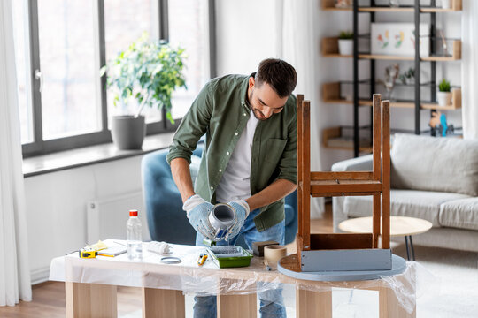 repair, diy and home improvement concept - man in protective gloves pouring grey color paint to tray for painting old wooden table