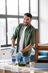 repair, diy and home improvement concept - happy smiling man in protective gloves stirring can with grey color paint for painting old wooden table