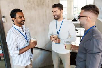 Fototapeta premium business, people and corporate concept - happy smiling businessmen or male colleagues with name tags drinking takeaway coffee at office