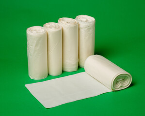 Five rolls of biodegradable eco plastic white garbage bags on green background.