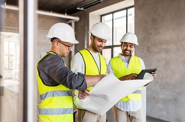 architecture, construction business and people concept - male architects in helmets with blueprint and tablet pc computer working in office building