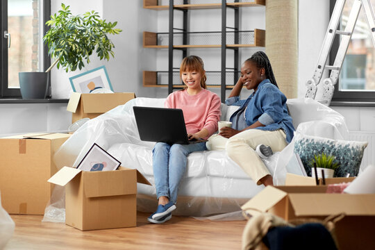 moving, people and real estate concept - happy smiling women with laptop computer and boxes at new home