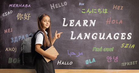 Schoolgirl with a backpack and book pointing at a blackboard in a foreign language school