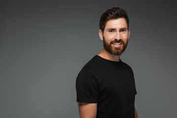 portrait of smiling bearded man in black t-shirt looking at camera isolated on grey.
