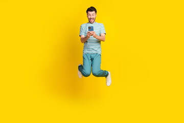 Full size photo of ecstatic impressed guy striped t-shirt blue pants sneakers look on phone jumping...