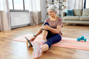 sport, fitness and healthy lifestyle concept - smiling senior woman exercising with tablet pc computer on mat at home
