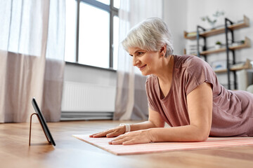 sport, fitness and healthy lifestyle concept - smiling senior woman with tablet pc computer exercising on mat at home