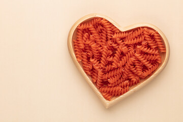 Red lentil fusilli pasta in a heart shaped wood bowl.